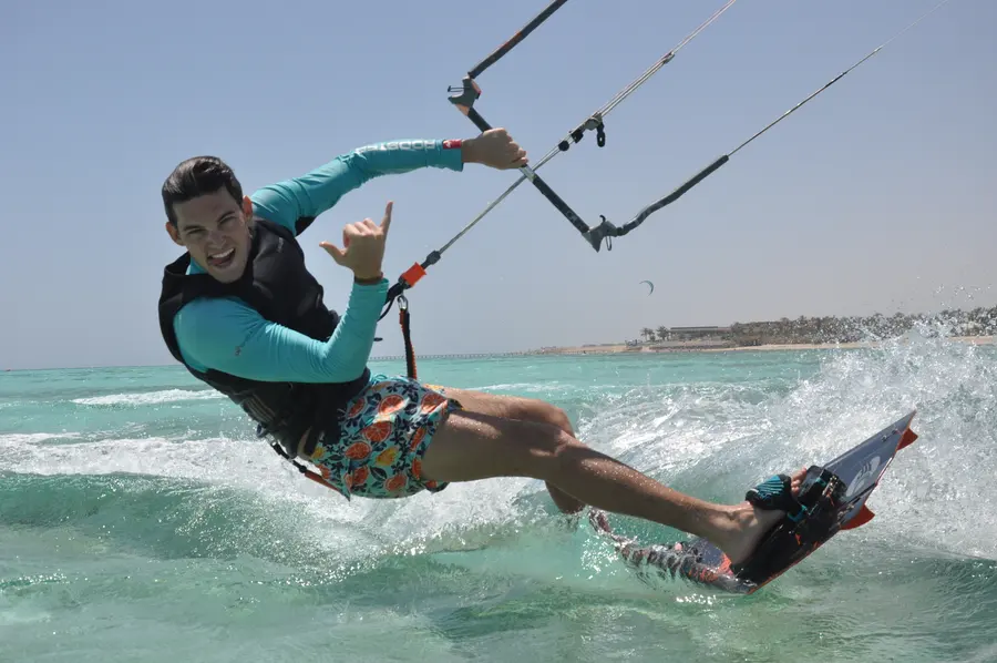 Rider in a long-sleeved rash top, vest and harness carving a turn on a twintip, with the bar and lines in view